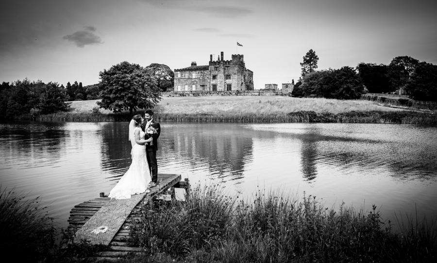 A couple embracing on a dock by a lake with a castle in the background.