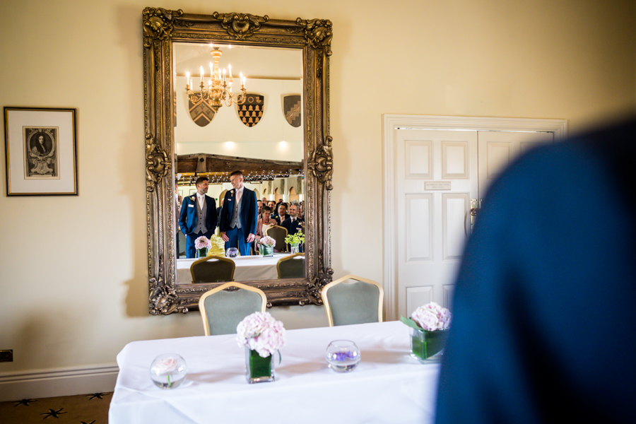 A group of people reflected in an ornate mirror in an elegant room with decorative elements.