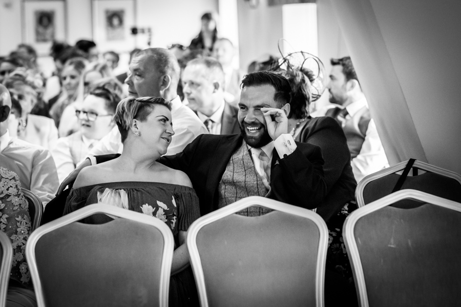 A couple sharing a joyful moment at a formal event with guests seated around them.
