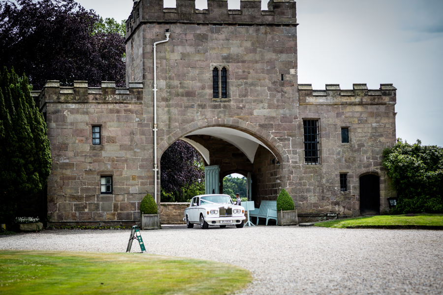 Classic car driving through an archway of a historical stone gatehouse.