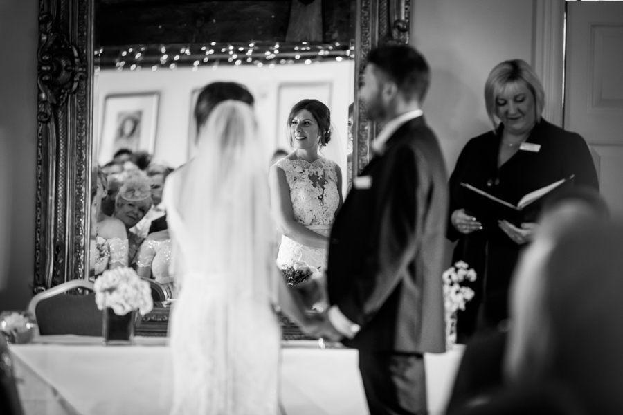 Bride and groom facing each other during wedding ceremony with an officiant in the background.