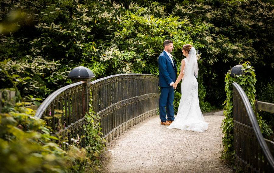Bride and groom holding hands on a bridge surrounded by greenery.
