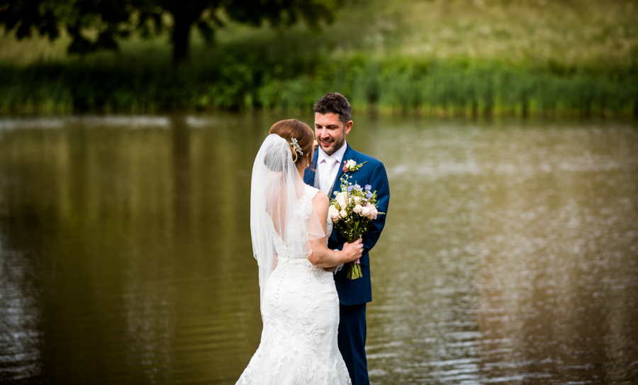 Bride and groom embracing by a lakeside.