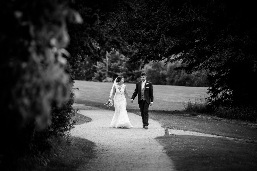 Bride and groom walking hand in hand on a park path in black and white photography.