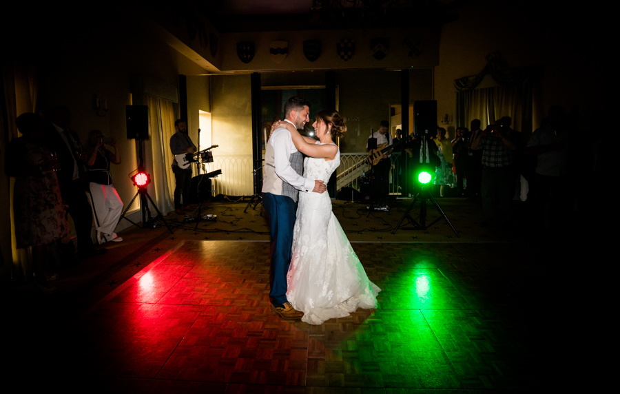 Couple sharing a dance at a wedding reception with colorful lights in the background.