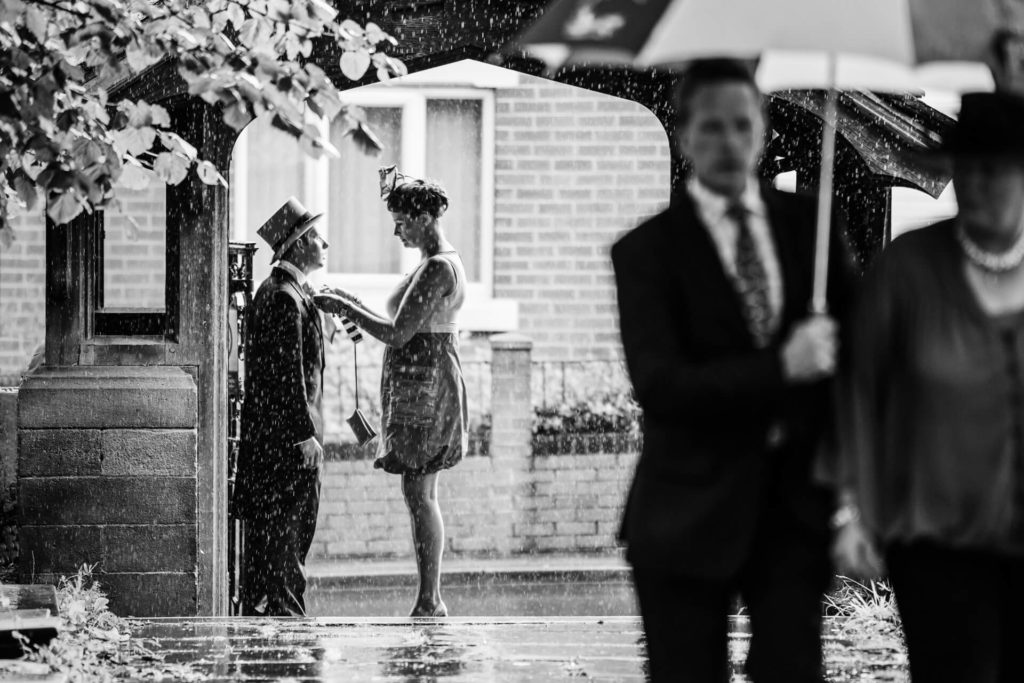 bridesmaid fixing a groomsman tie under the church archway in the rain