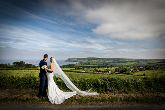 A bride and groom, Rachel & TJ, standing on a hill overlooking the sea.