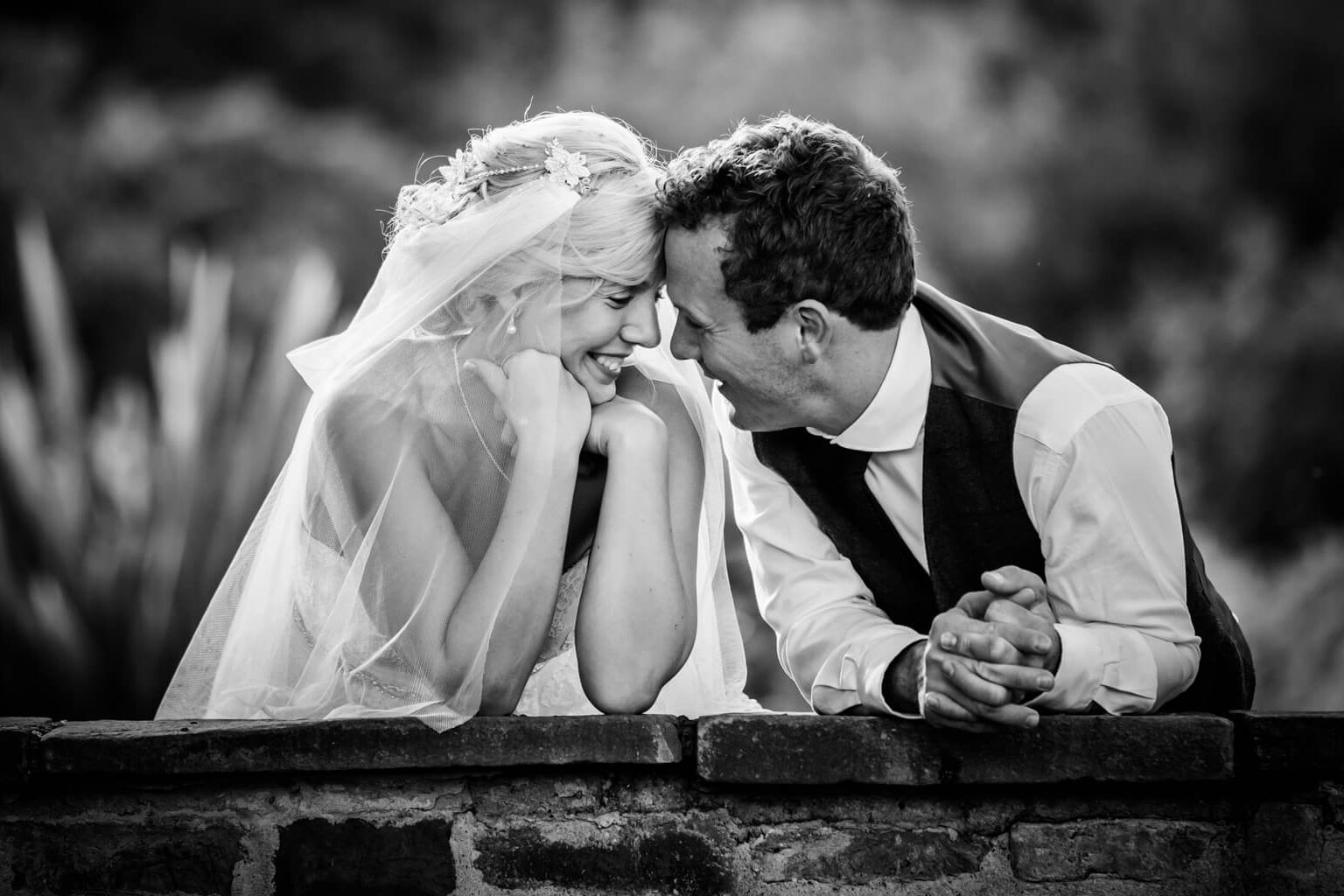 bride and groom leaning on a wall and laughing together