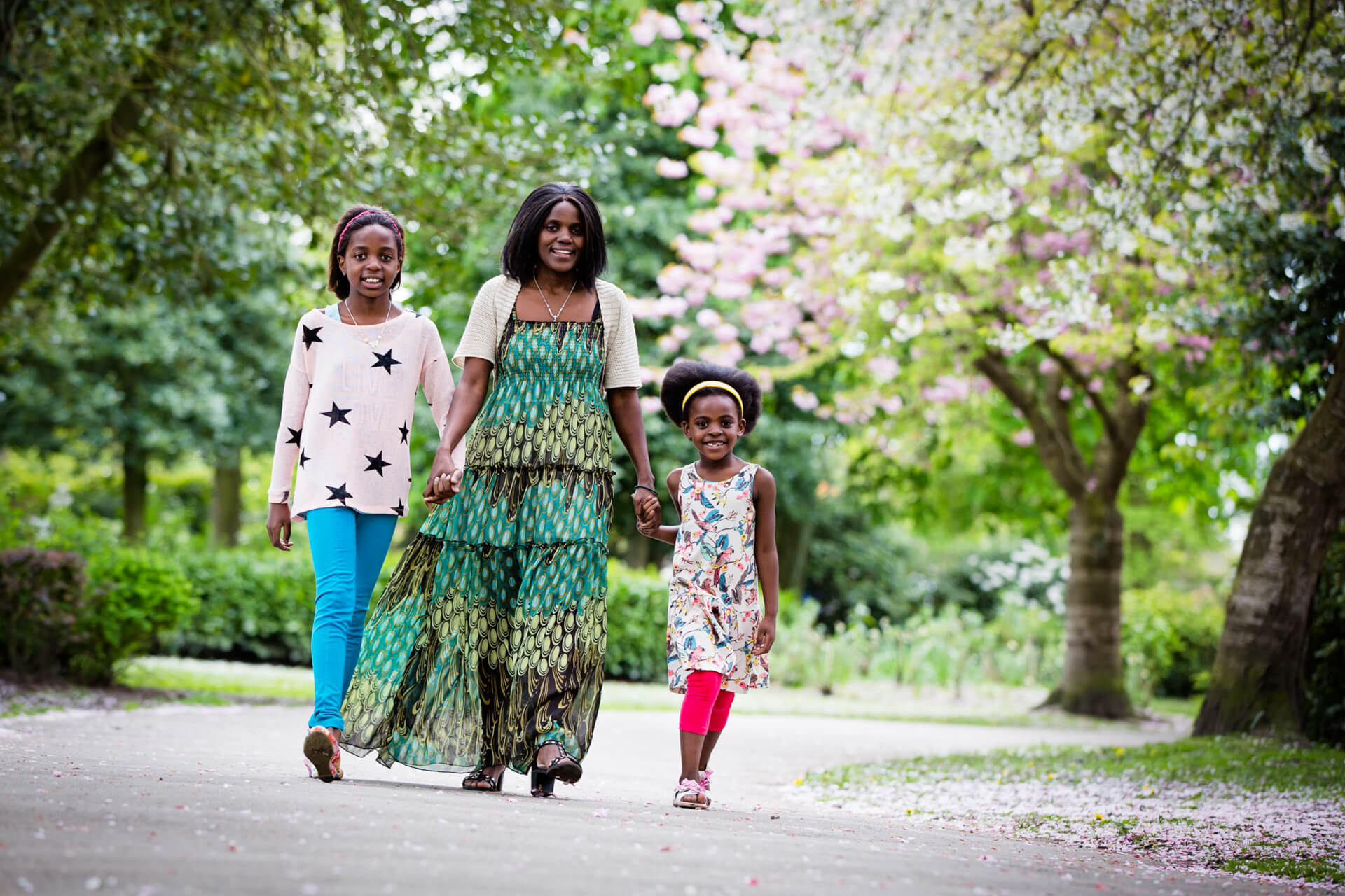 A mother and two daughters walking down a path in a park.