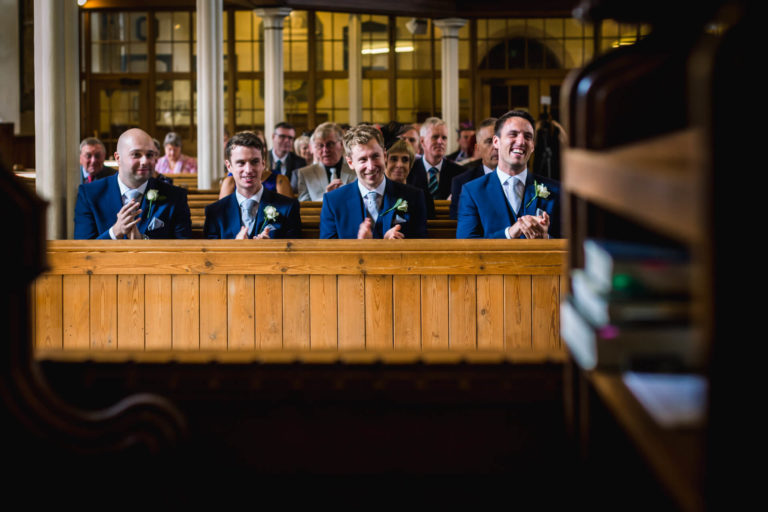 Groomsmen smiling and applauding during a wedding ceremony.