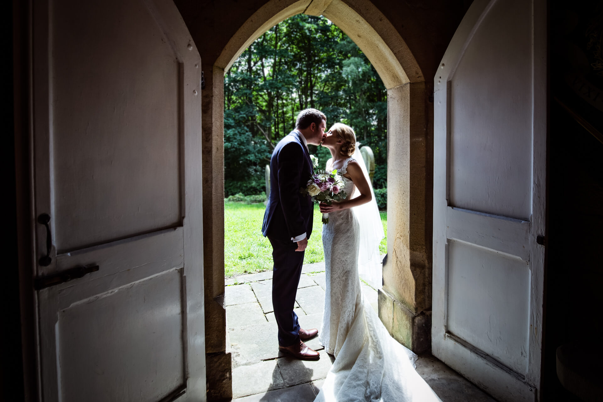 Bride and Groom kissing in the church doorway at Denton Hall