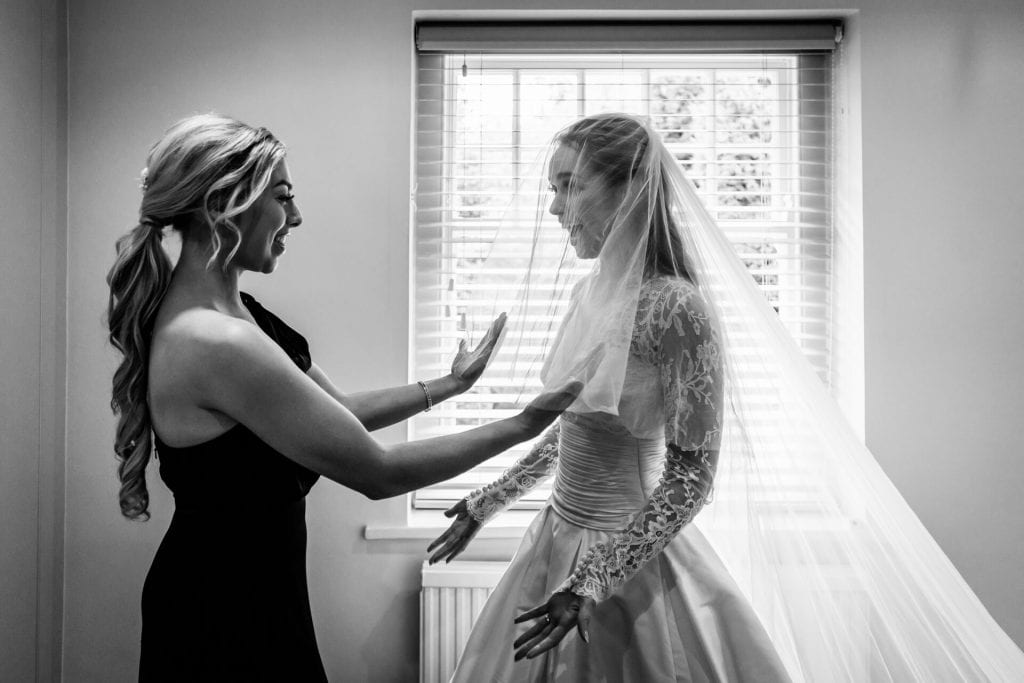 bride and bridesmaid laugh whilst putting on the veil