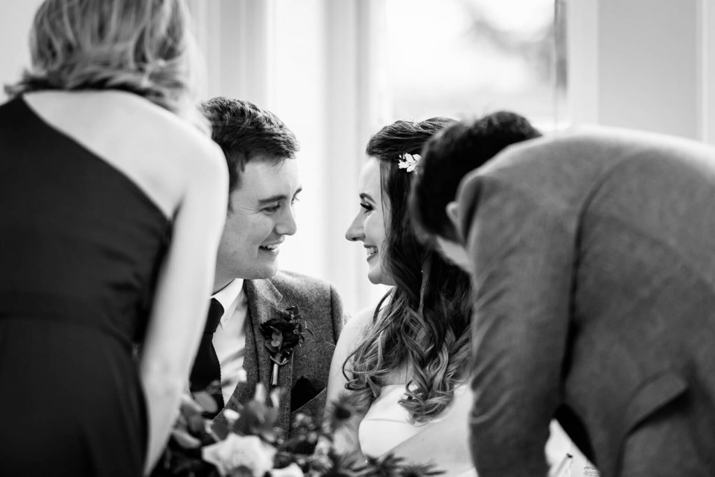 bride and groom smile at each other whilst their witnesses sign the wedding register