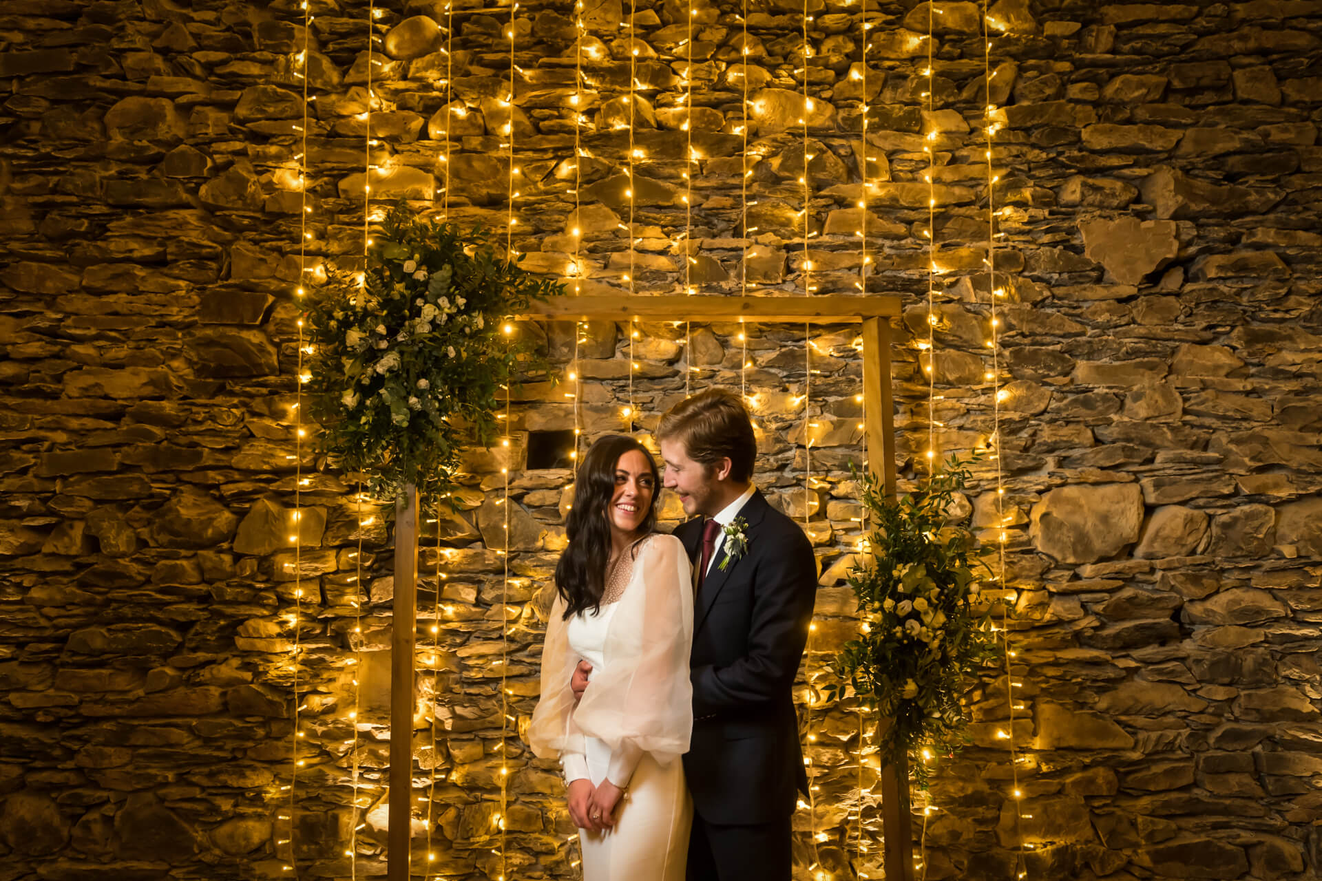 wedding couple hugging in front of a wall of fairy lights