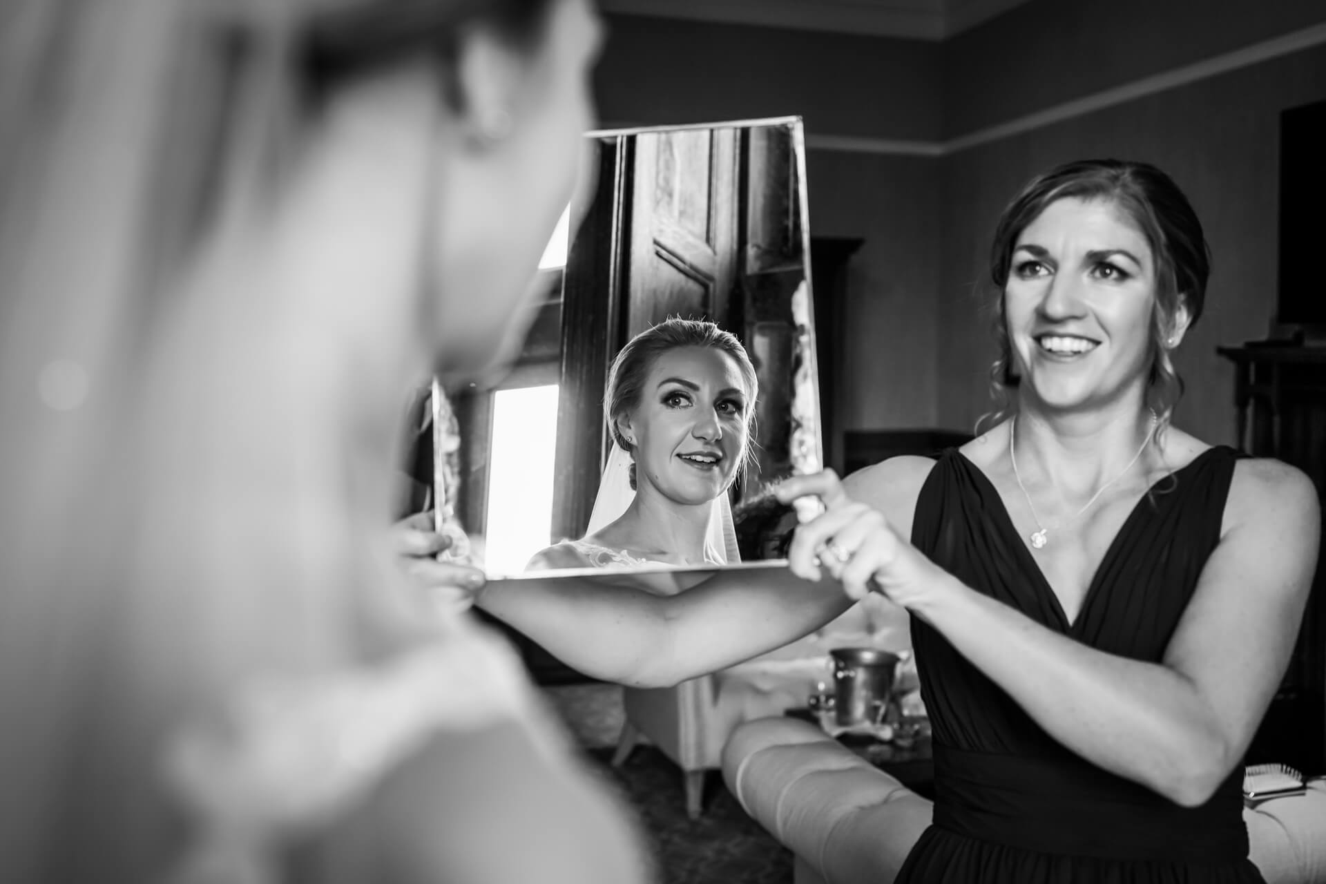 bride looks in a mirror being held by her bridesmaid