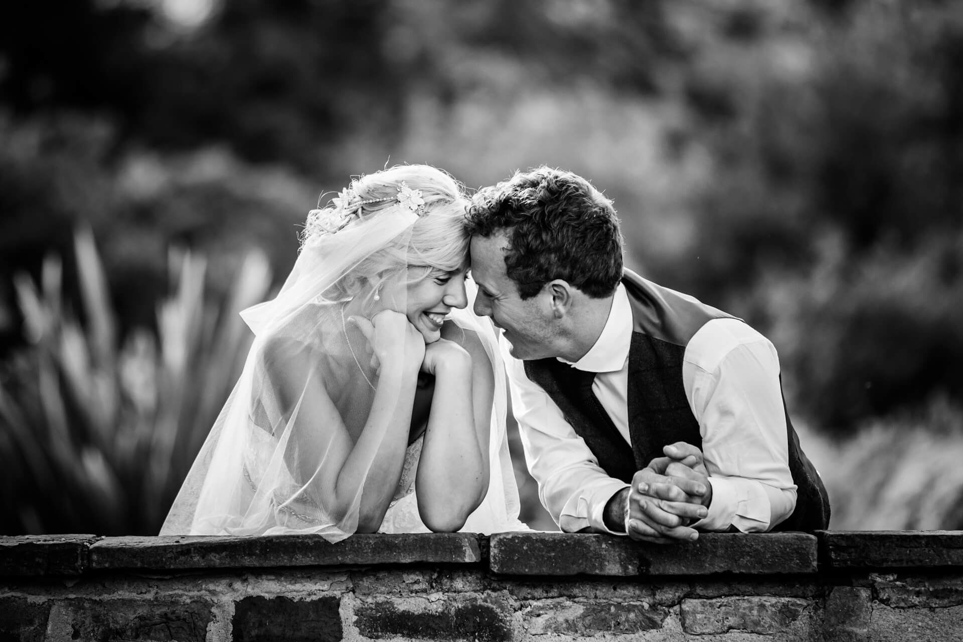 bride and groom smile at each other whilst leaning on a wall at Hornington Manor