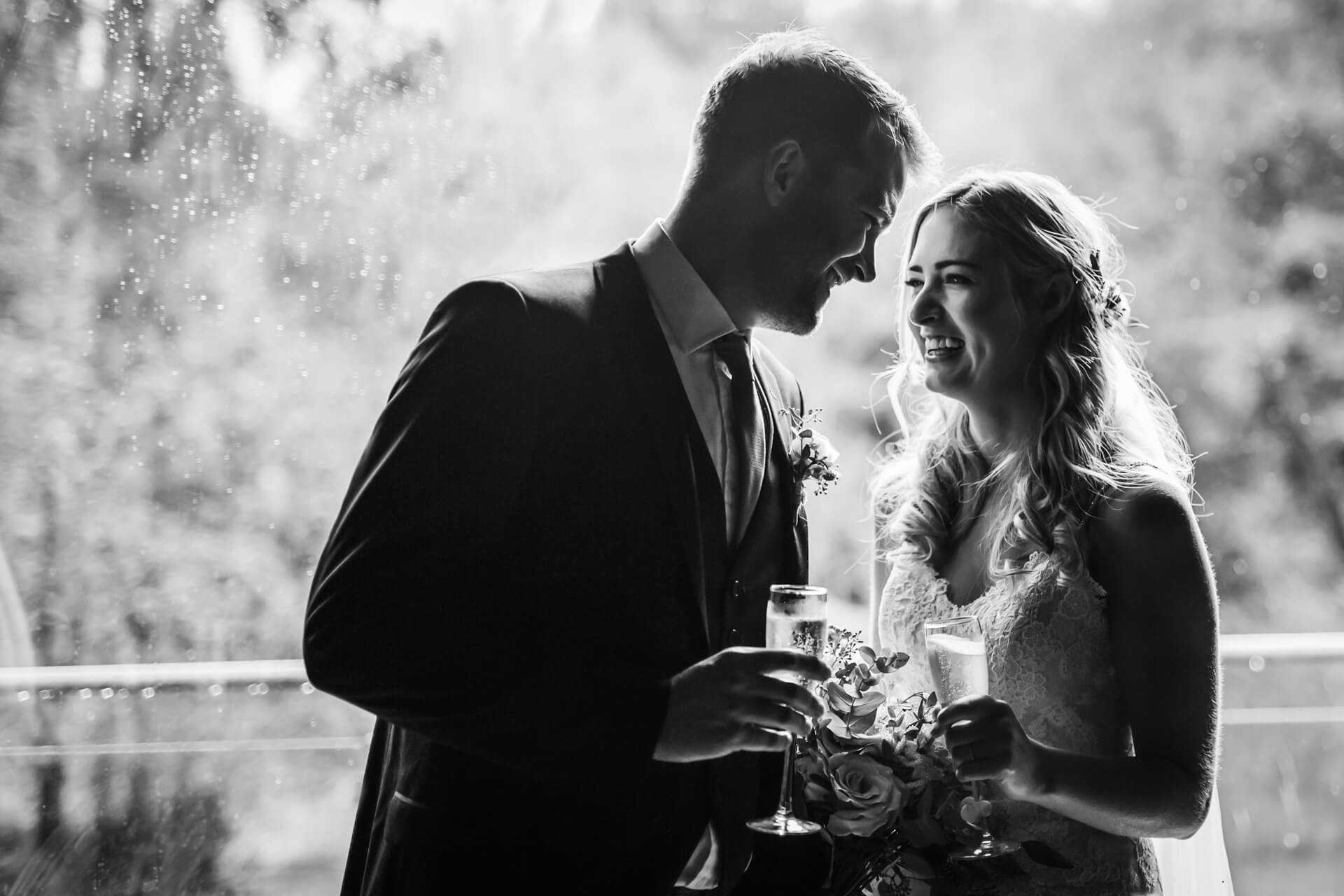 bride and groom smile at each other whilst holding champagne glasses