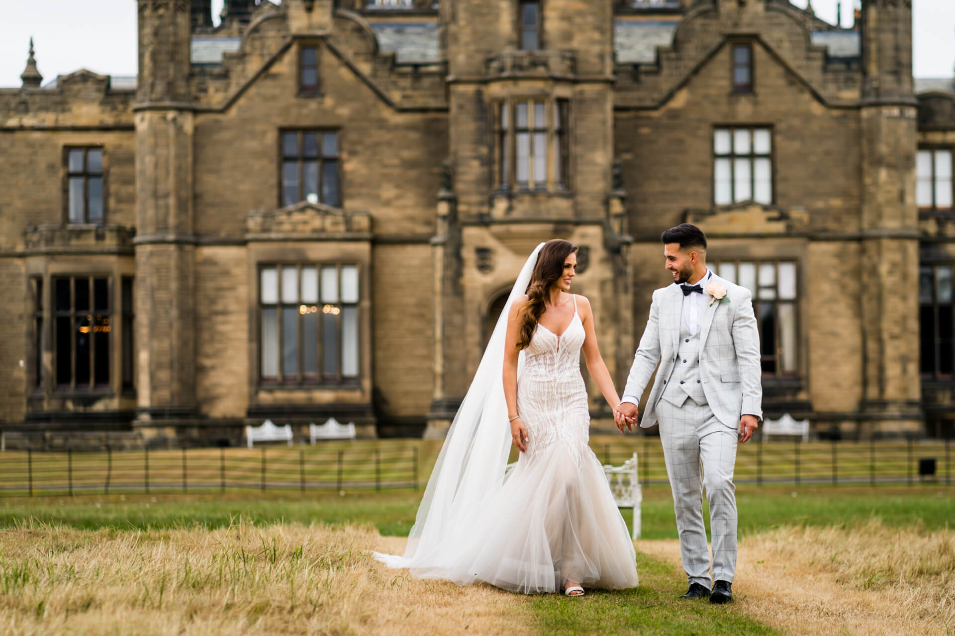 bride and groom walking together in front of Allerton castle