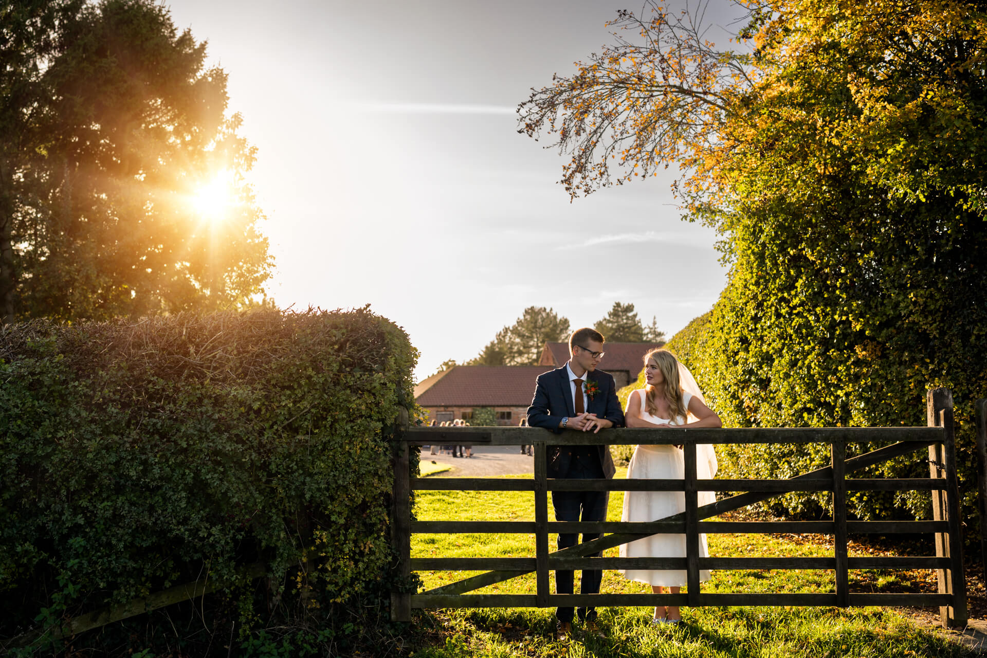 bride and groom leaning on a gate in front of Woolas barn