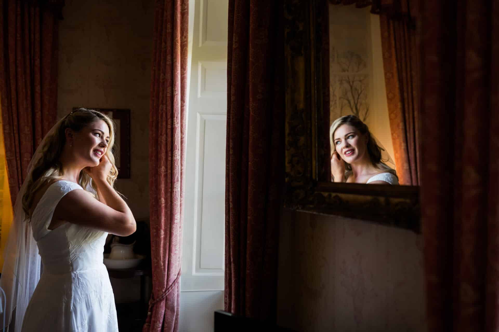 brides reflection in a mirror as she puts her earrings in