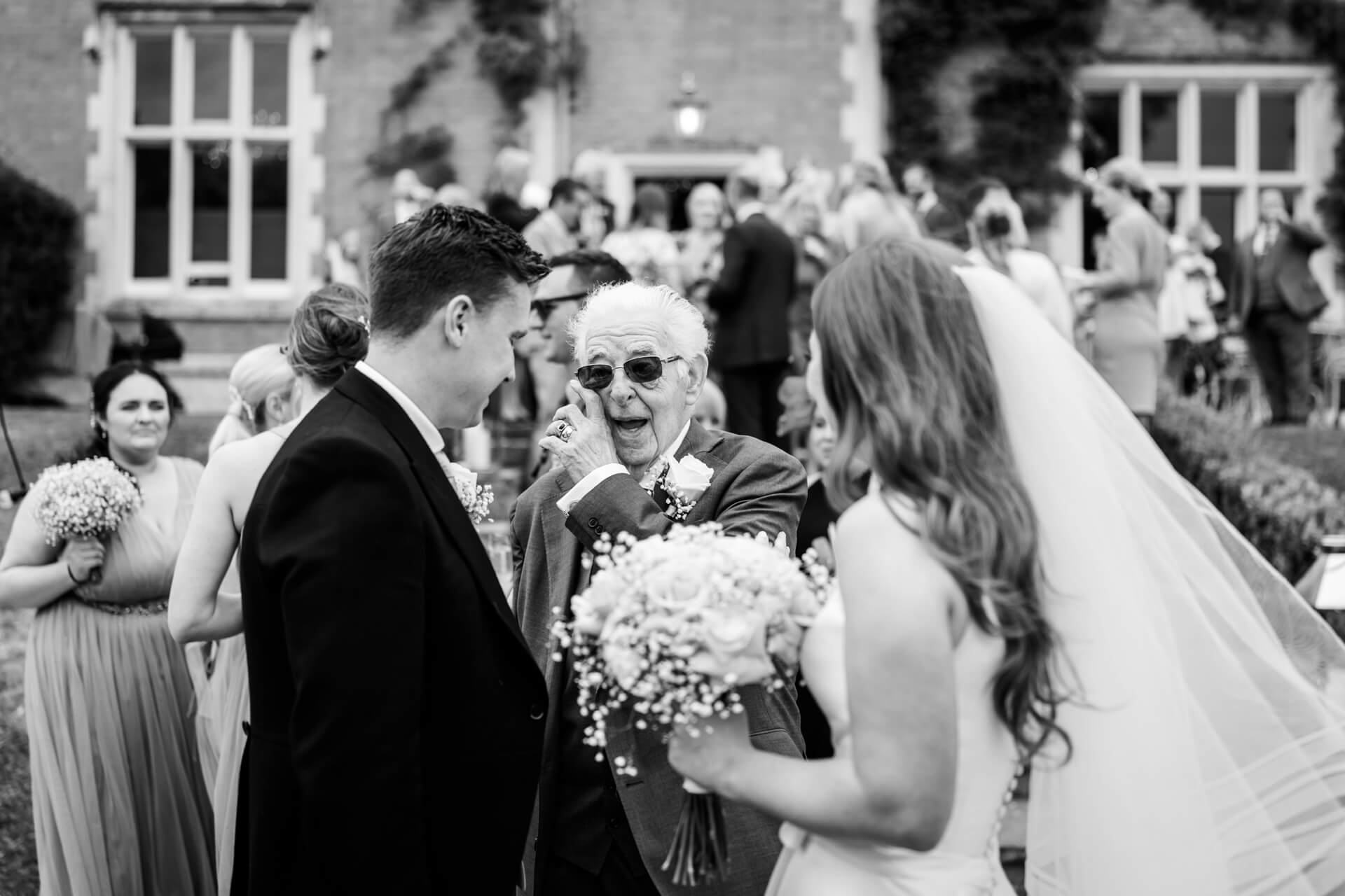 grandad wiping a tear from his eye whilst talking to the bride and groom
