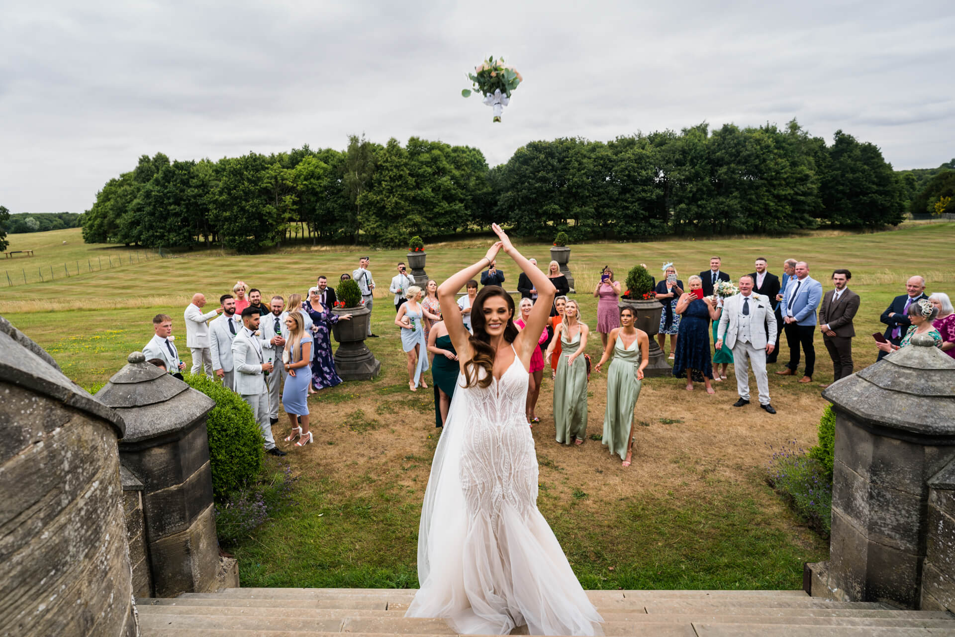 bride throwing her bouquet on the steps of Allerton castle