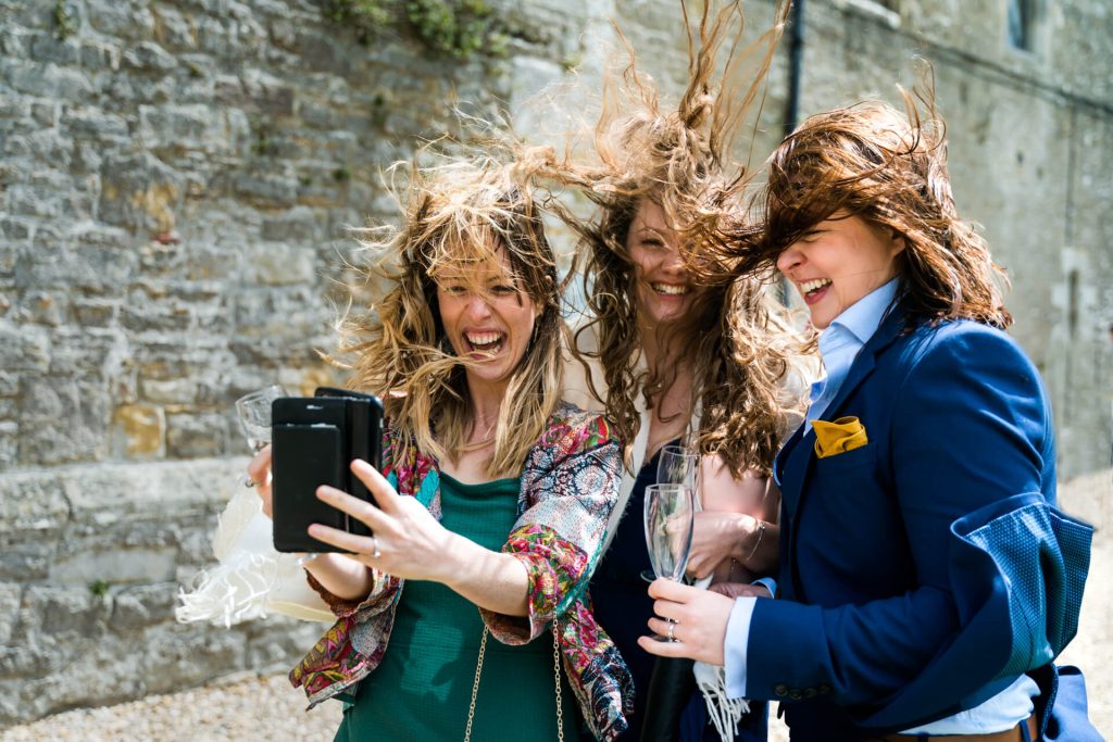 wedding guests laughing whilst their hair is blow by very strong winds
