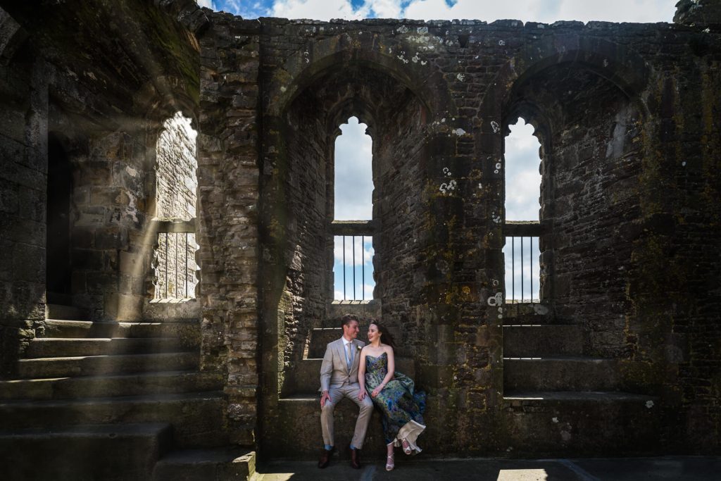 Bride and groom sitting on a window ledge inside Bolton Castle