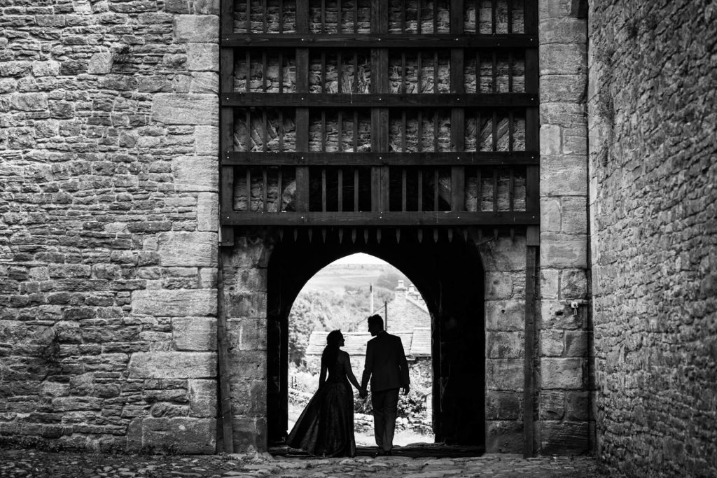 Silhouette of the bride and groom walking through the portcullis at Bolton Castle