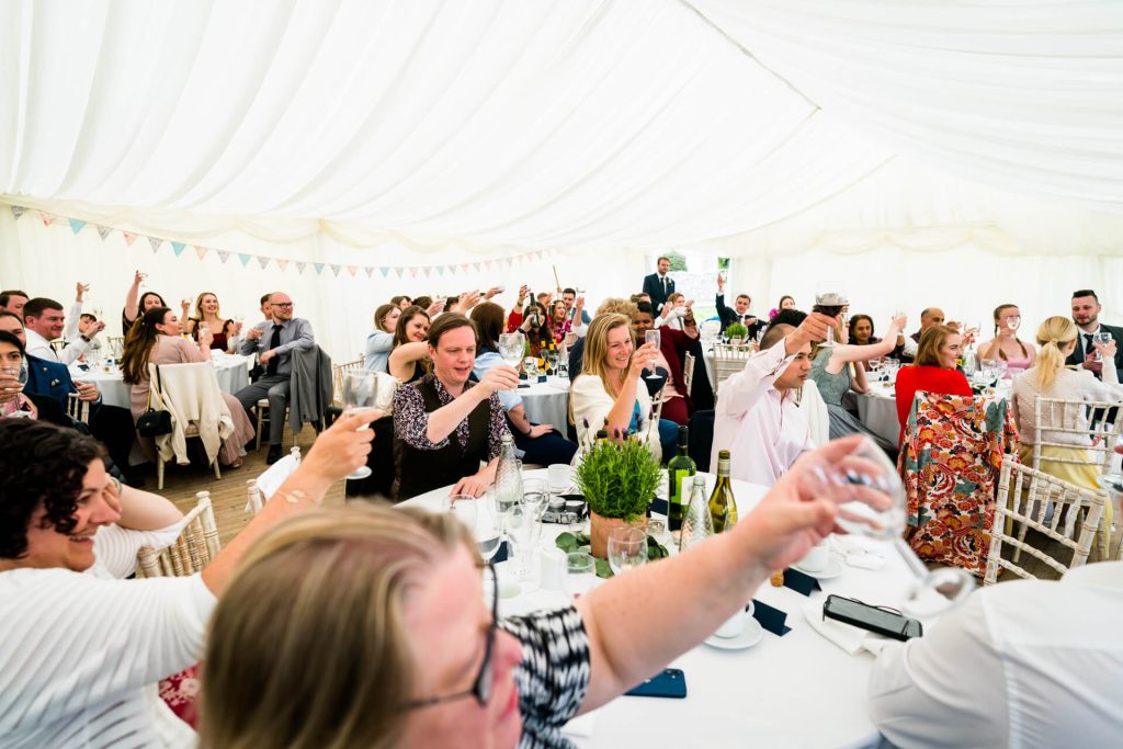 a marquee full of wedding guests cheering after the speeches