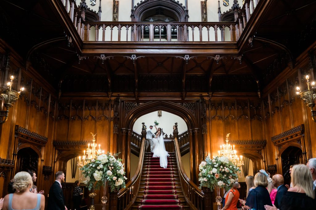 bride and groom wave to their guests as they leave via the grand staircase