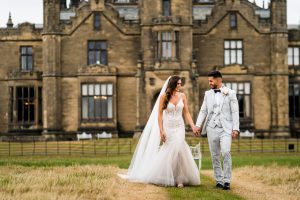 bride and groom walking whilst holding hands in front of Allerton Castle