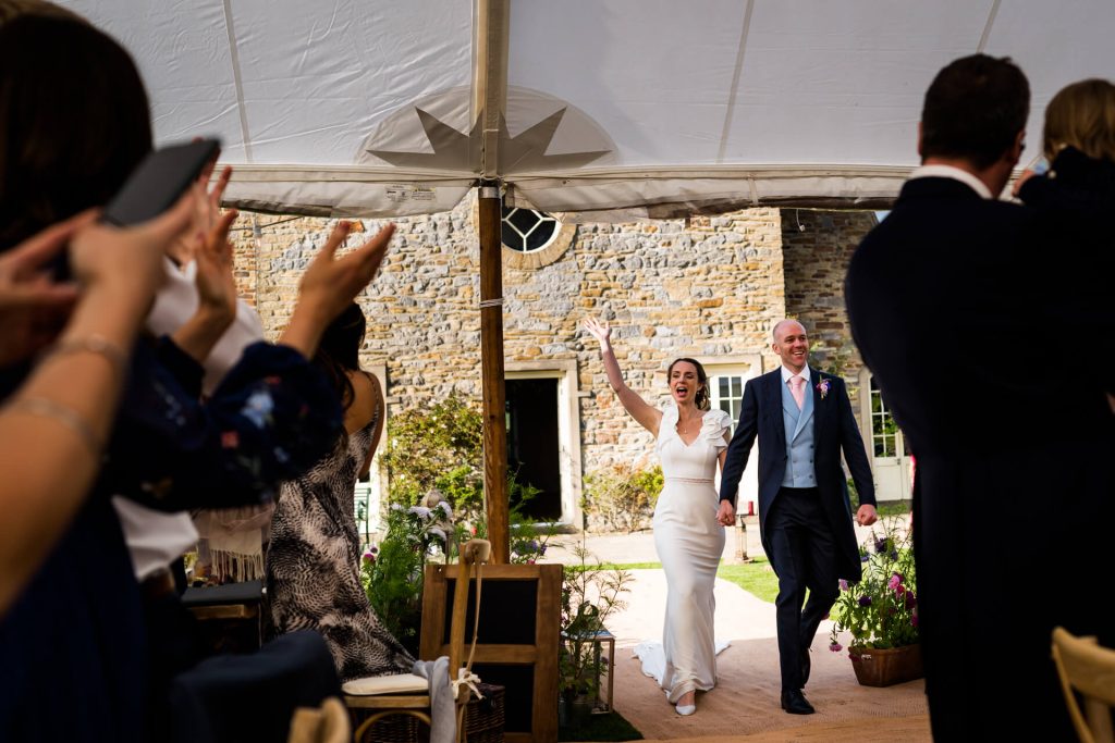wedding couple celebrate with arms in the air as they enter the marquee