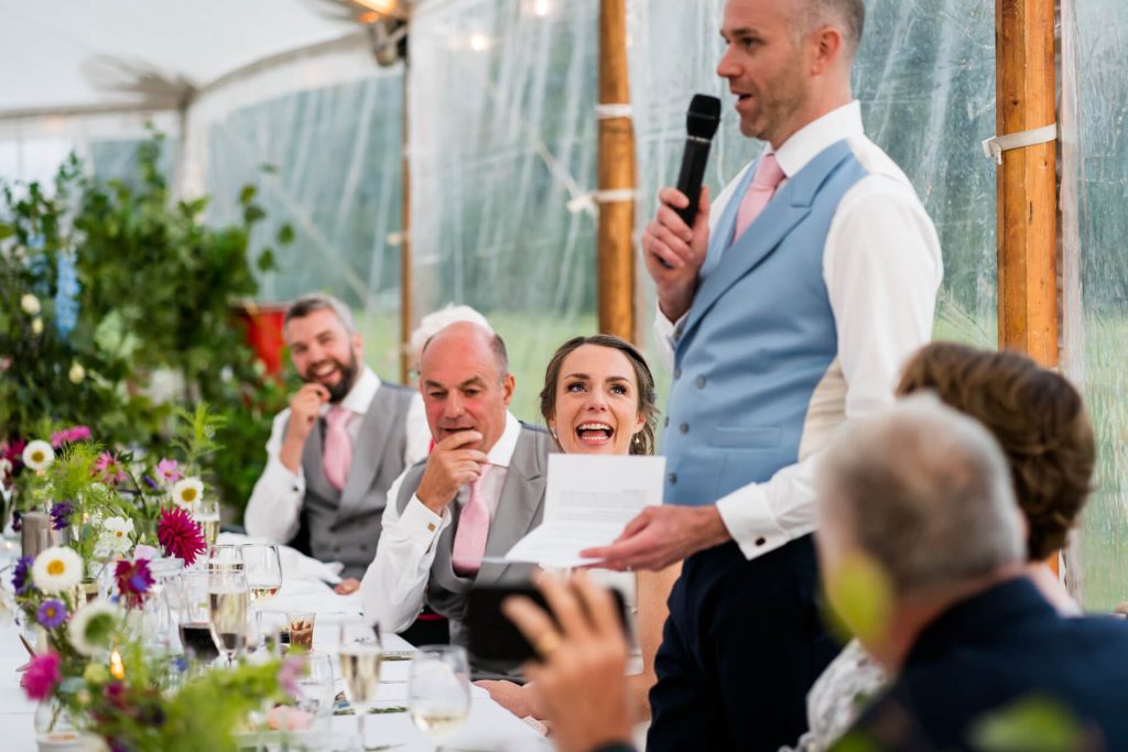 bride laughing at the groom as he gives his speech