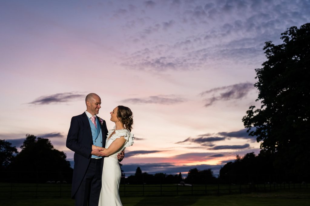 portrait of the wedding couple in front of a sunset on the Broughton Hall Estate