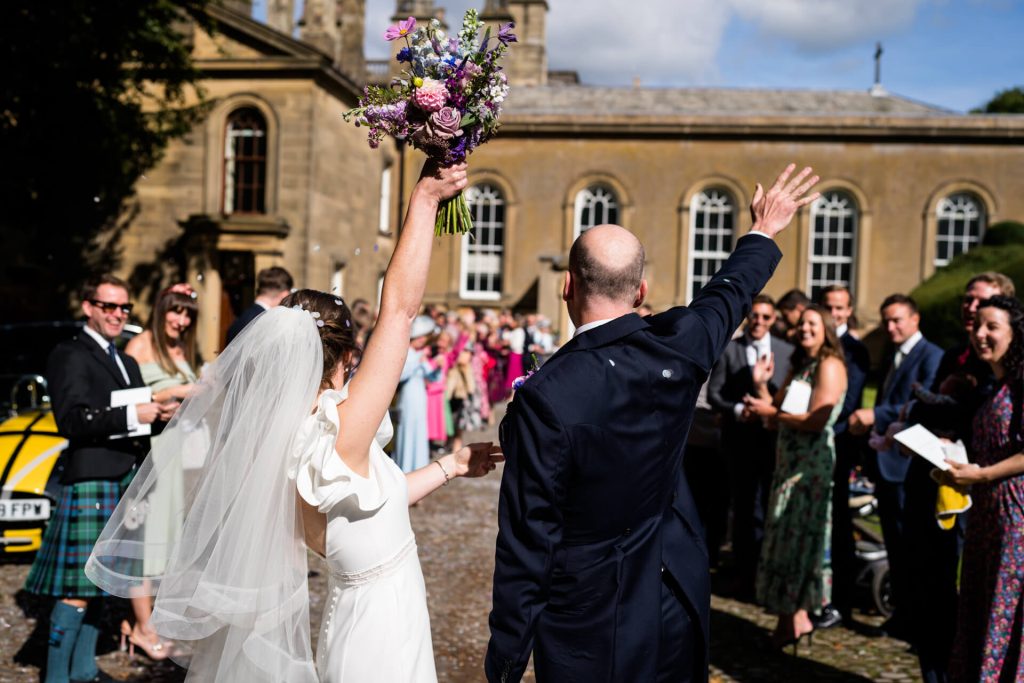 bride and groom waving at all of their guests outside the church