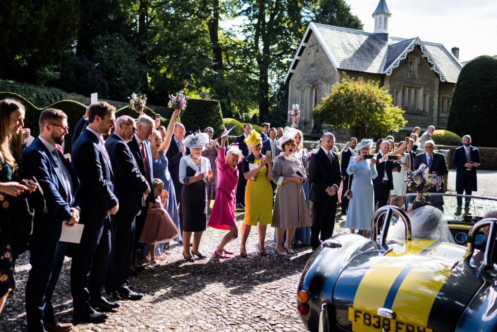wedding guests cheering as the wedding couple leave the church in their car