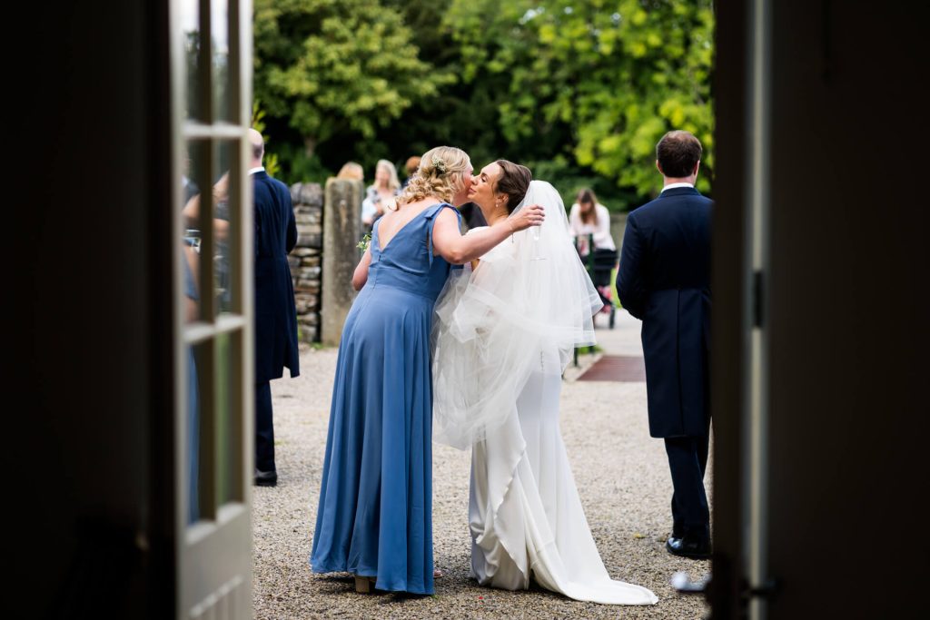 view through a doorway of the bride kissing a bridesmaid