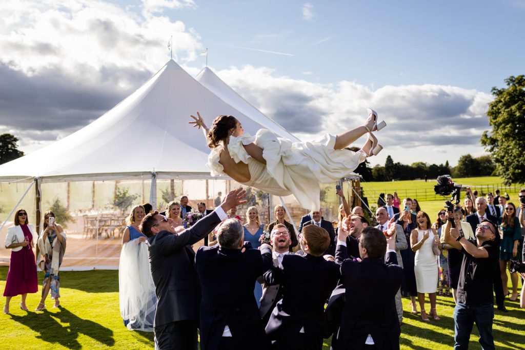 a group of groomsmen throwing the bride in the air on the Broughton Hall Estate