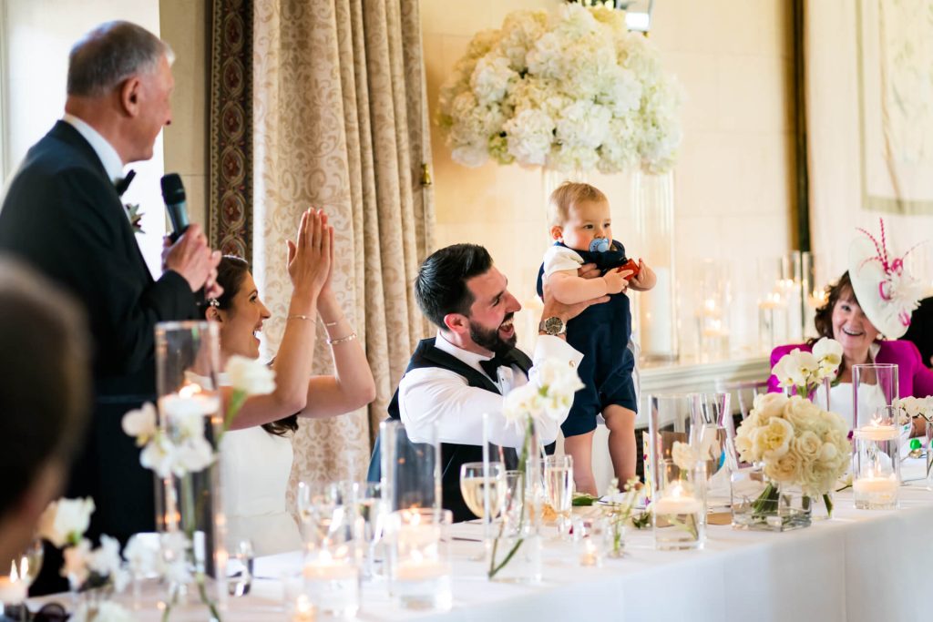 groom raising his baby boy in the air at top table
