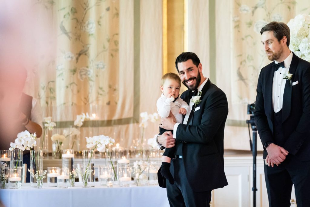 groom and his baby boy smiling at the top of the wedding aisle