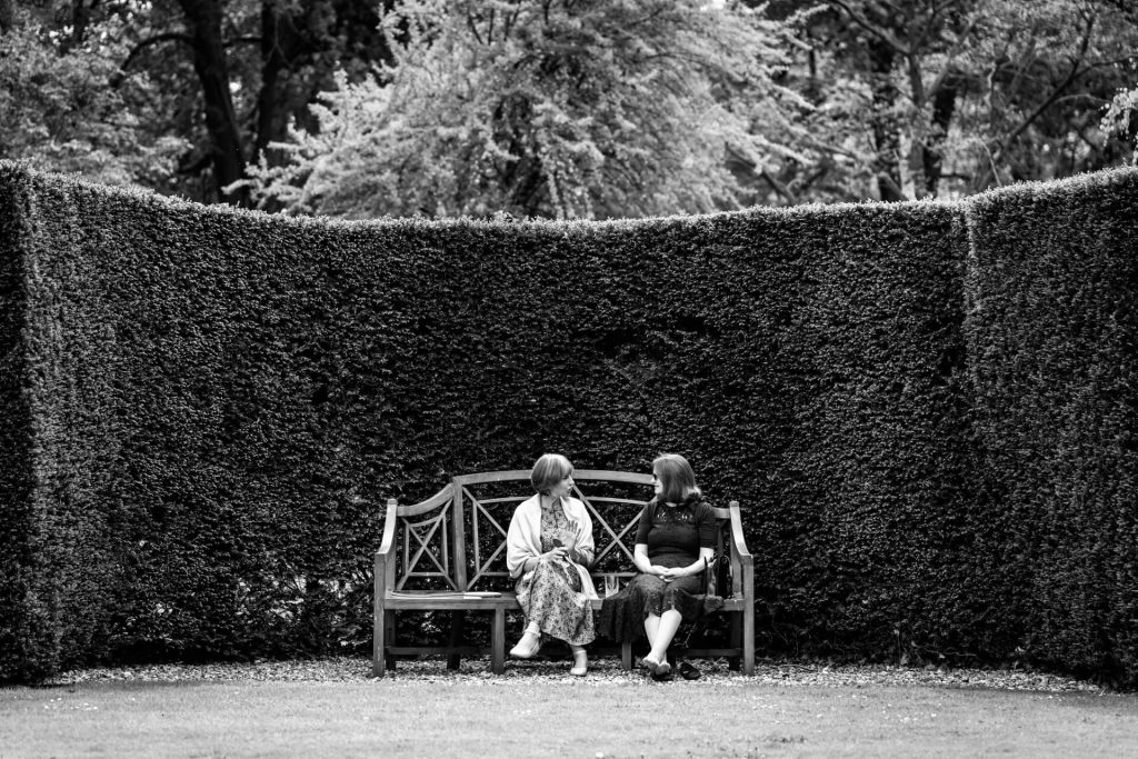 two wedding guests sitting on a garden bench chatting