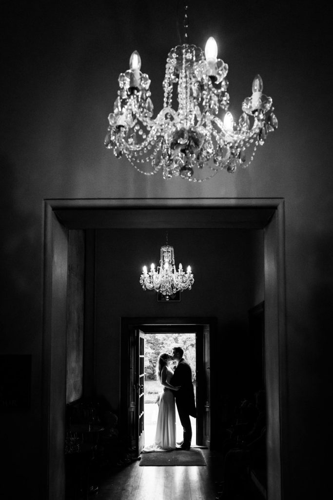 bride and groom kissing in a doorway under some chandeliers at Thicket Priory