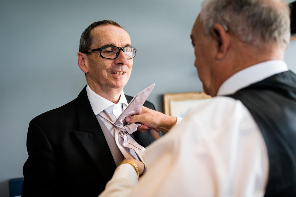 father of the bride having his tie fixed by a groomsman