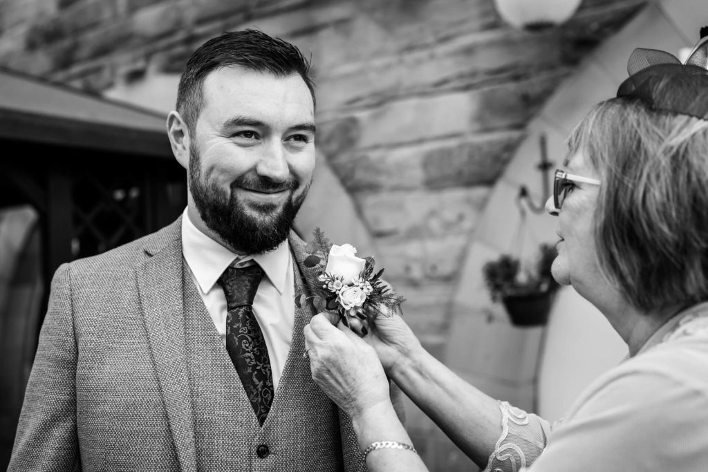 groom smiling whilst having his buttonhole attached