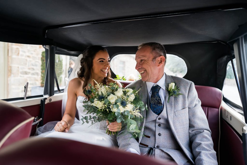 bride and her father smile at each other in the wedding car