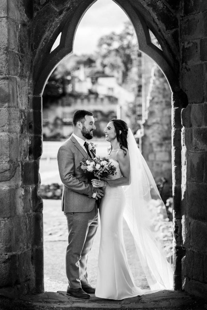 bride and groom standing together under an archway at the Bolton Abbey ruins