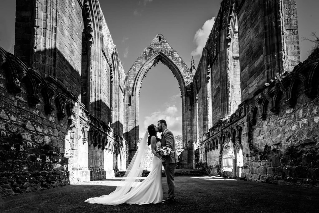 bride and groom kissing under a huge archway at Bolton Abbey