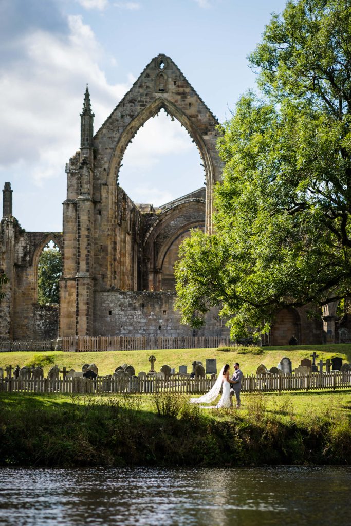 view from across the river of a wedding couple in the grounds of Bolton Abbey