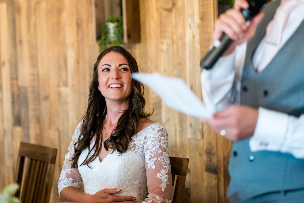 bride smiling at the groom during his wedding speech